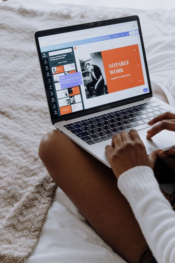 Close-up of hands using a laptop for presentation design on a cozy bed.